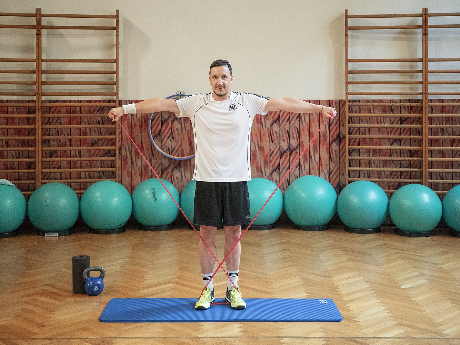 Erfahrunsgbericht Total Body Workout - Armtraining mit Gummibändern Kursteilnehmer nutzt Gummibänder für sein Armtraining, im Hintergrund liegen Gymnastik-Bälle